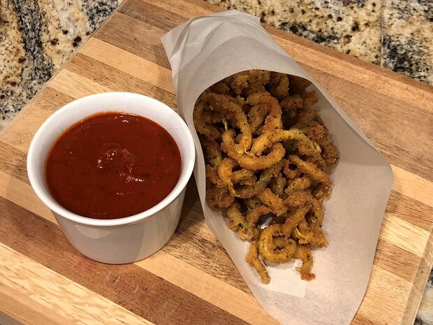 Packet of zucchini curly fries next to a dish of marinara dipping sauce